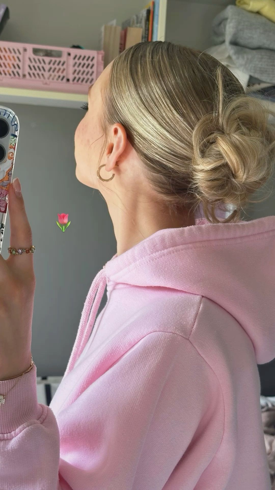 woman with messy bun in pink hoodie taking mirror selfie