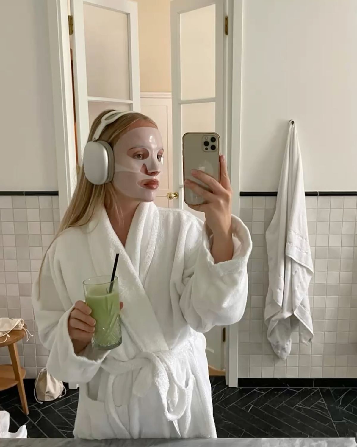 woman in robe with face mask and green juice self-care routine