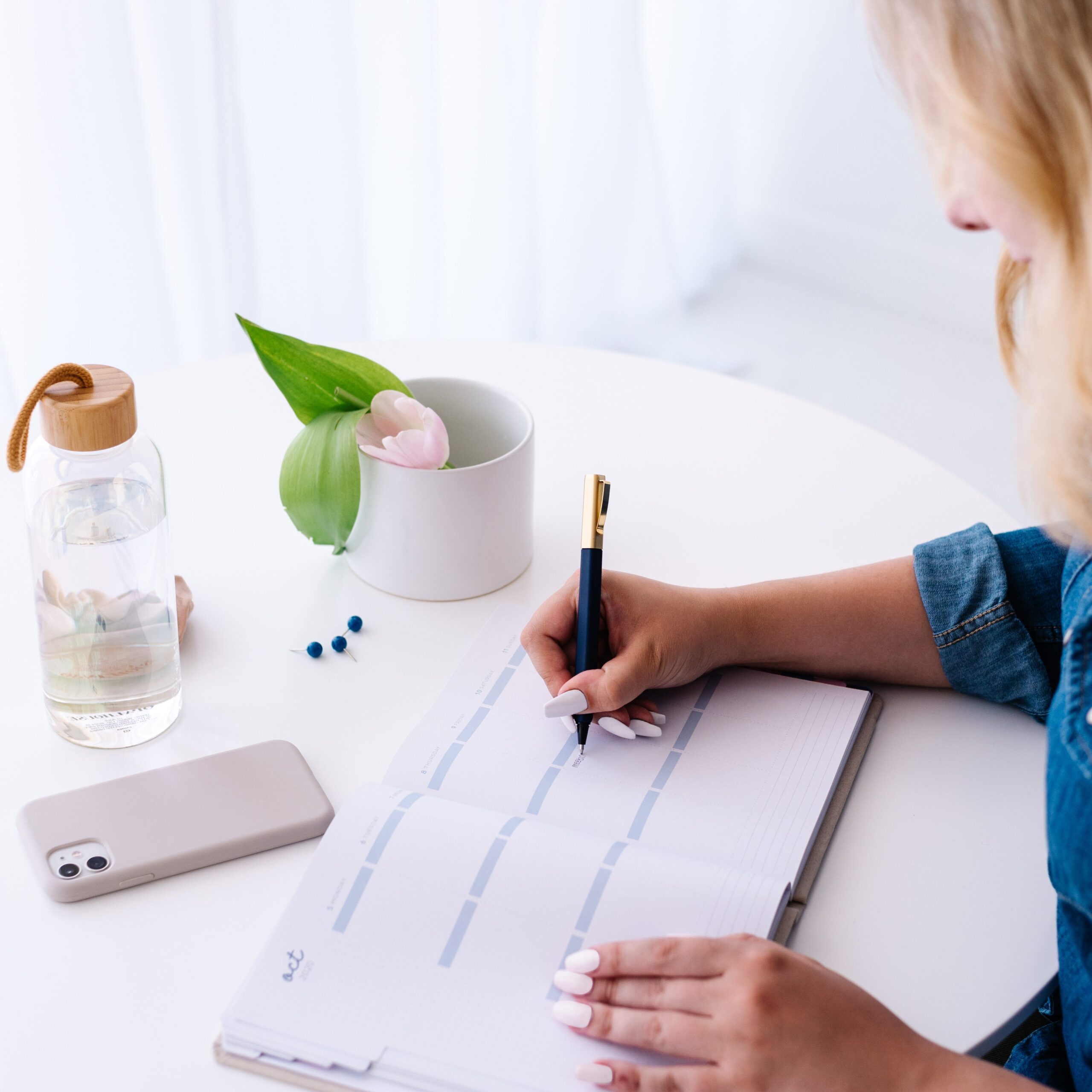 woman writing in planner at minimalist desk with flowers