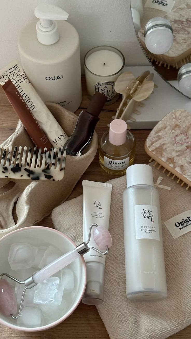 Facial skincare products, ice jade roller, spa candle, silk scrunchies and hair clips on wood table flat lay for beauty routine.