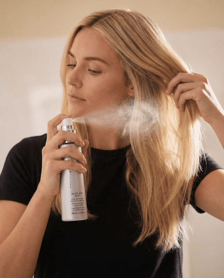 Woman applying heat protectant for thin blonde hair, using spray on long hair, hair care routine, black shirt.