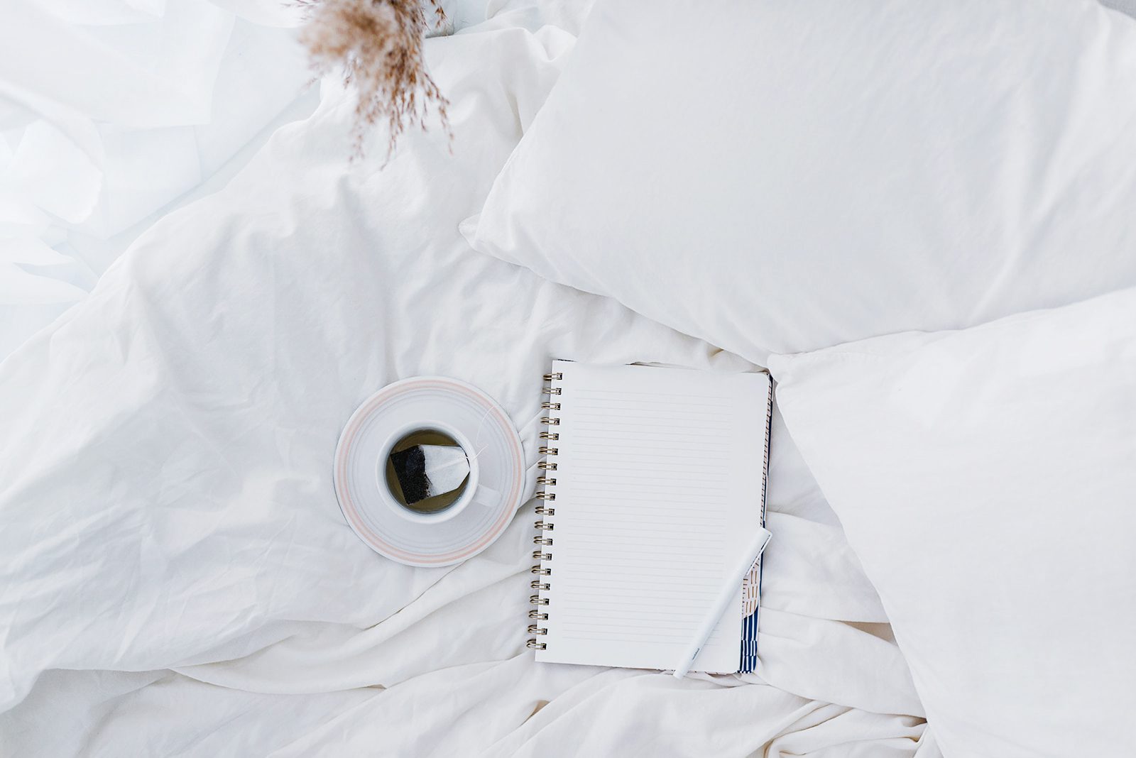 open notebook and coffee cup on white bed linens