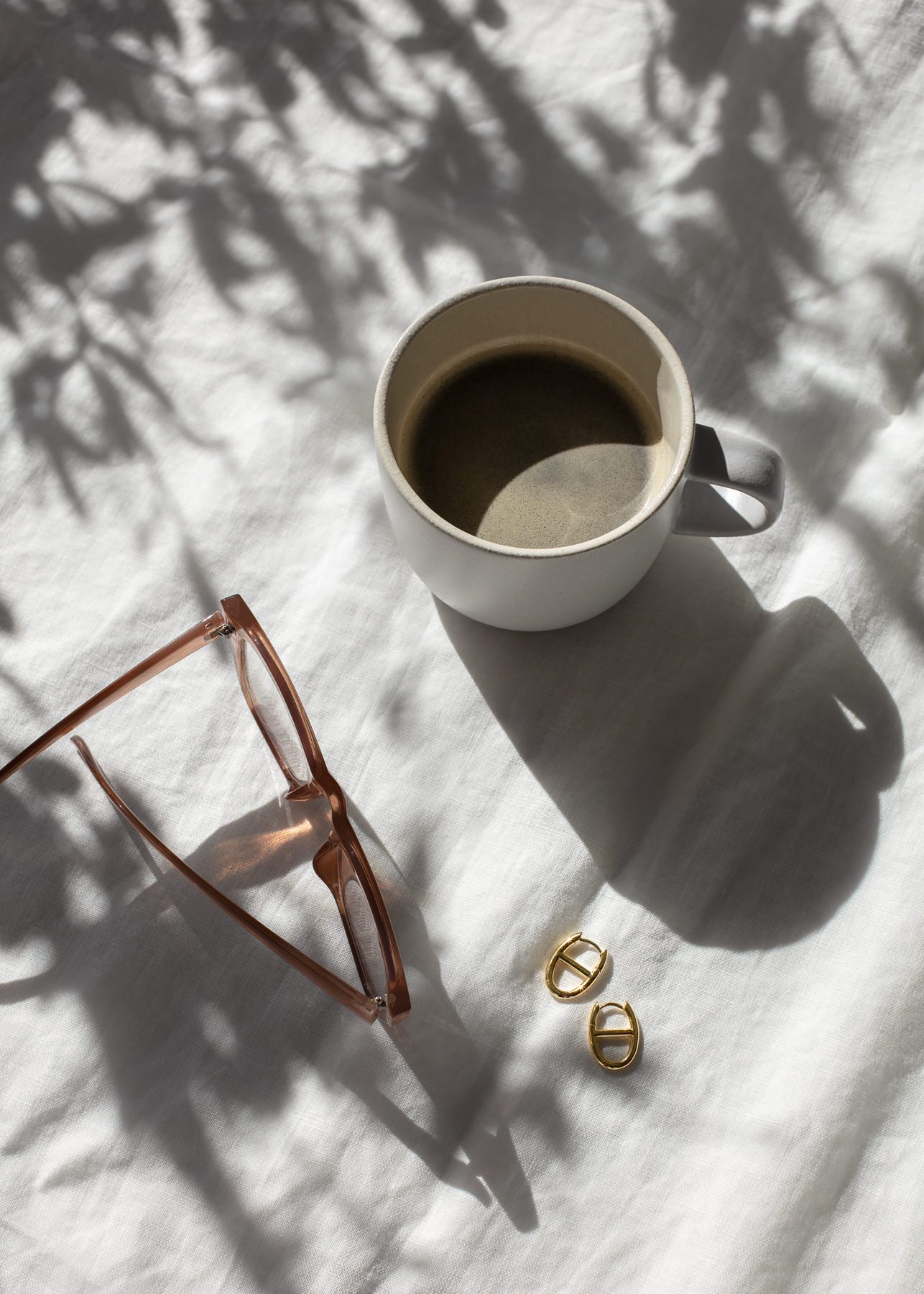 Coffee mug and reading glasses with morning light shadows for journaling routine