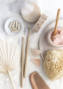 Natural spa essentials flat lay with organic soap bars, exfoliating scrub jar, bamboo toothbrushes, eco sponge, wooden comb, supplements.