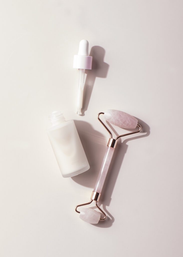 Anti-aging facial serum bottle with dropper and rose quartz face roller on pastel pink background, skincare beauty flatlay.