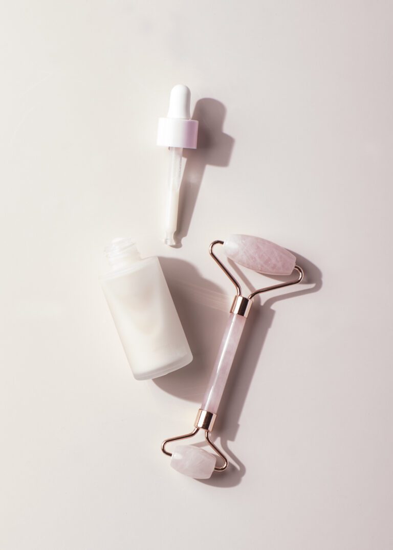 Anti-aging facial serum bottle with dropper and rose quartz face roller on pastel pink background, skincare beauty flatlay.