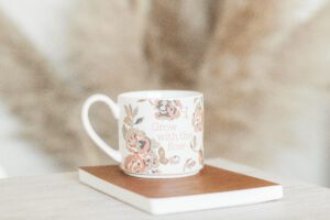 Inspirational floral coffee mug with “Grow with the flow” quote on closed book, cozy neutral background, home decor inspiration.
