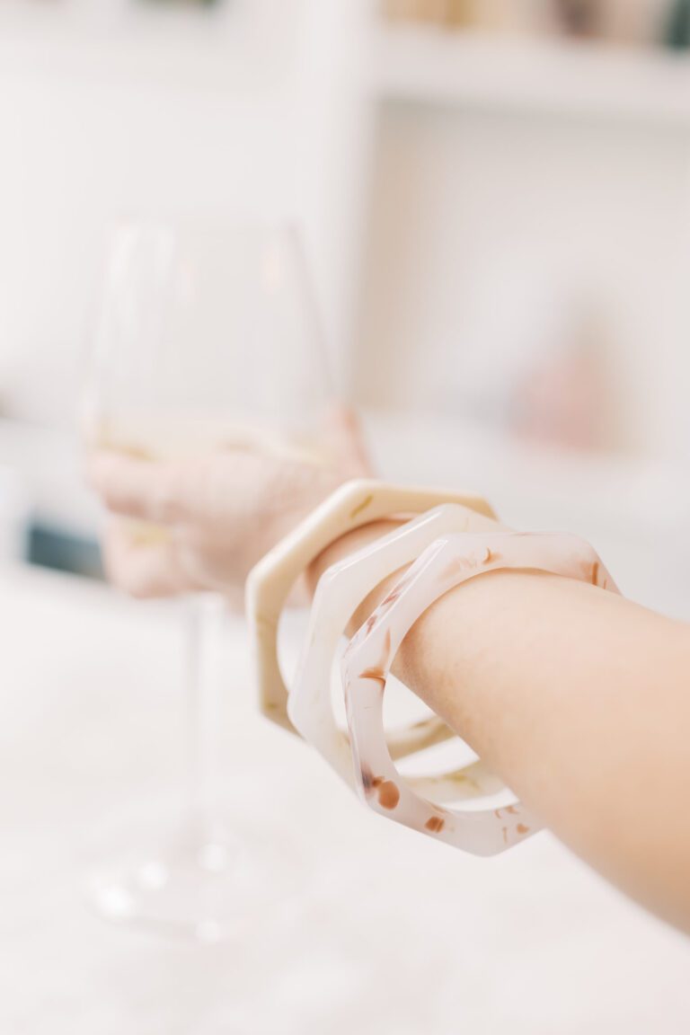 Trendy chunky resin bracelets on hand holding wine glass, minimalist jewelry aesthetic, blurred background, fashion accessory.