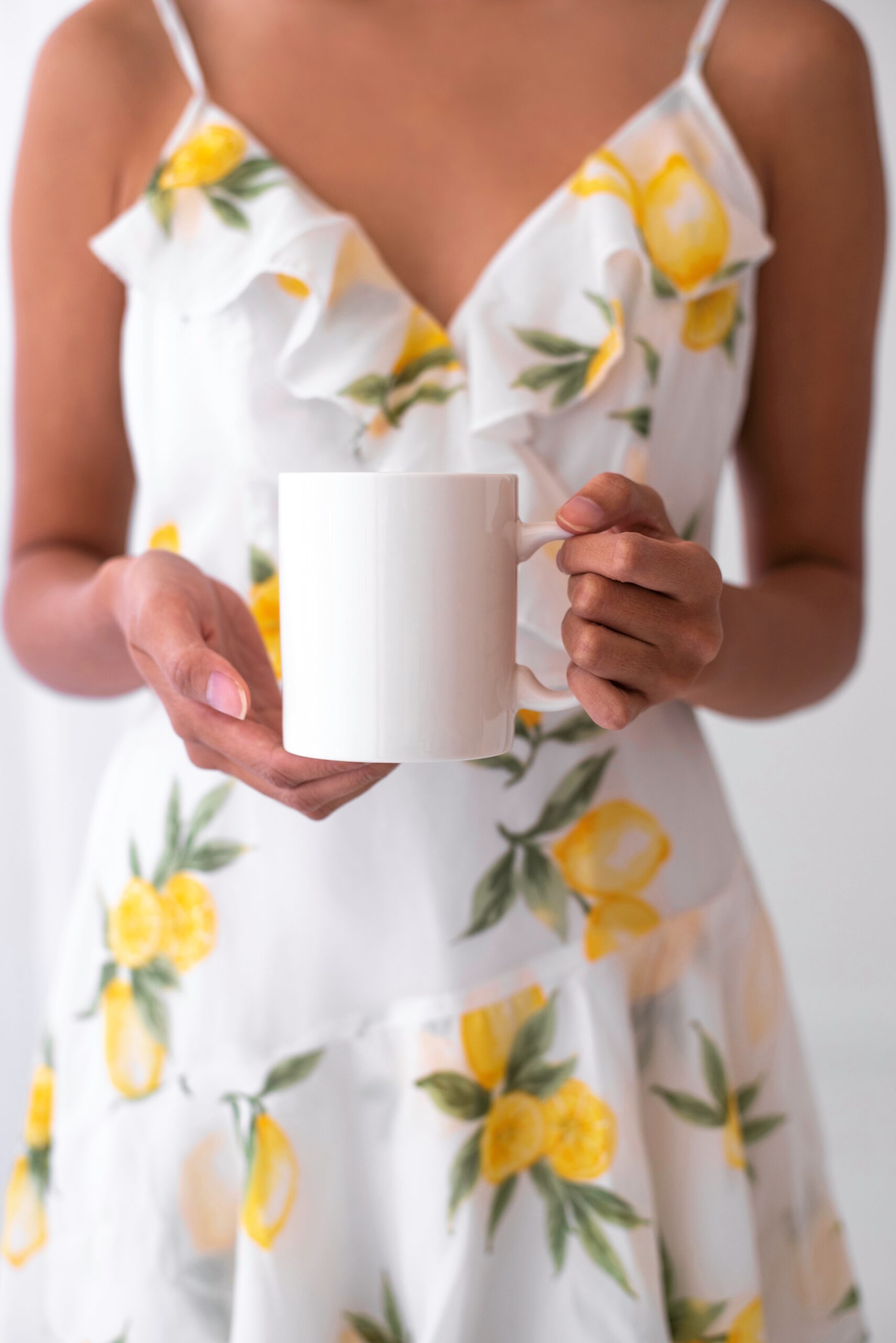woman in lemon print dress holding white mug butter yellow nails