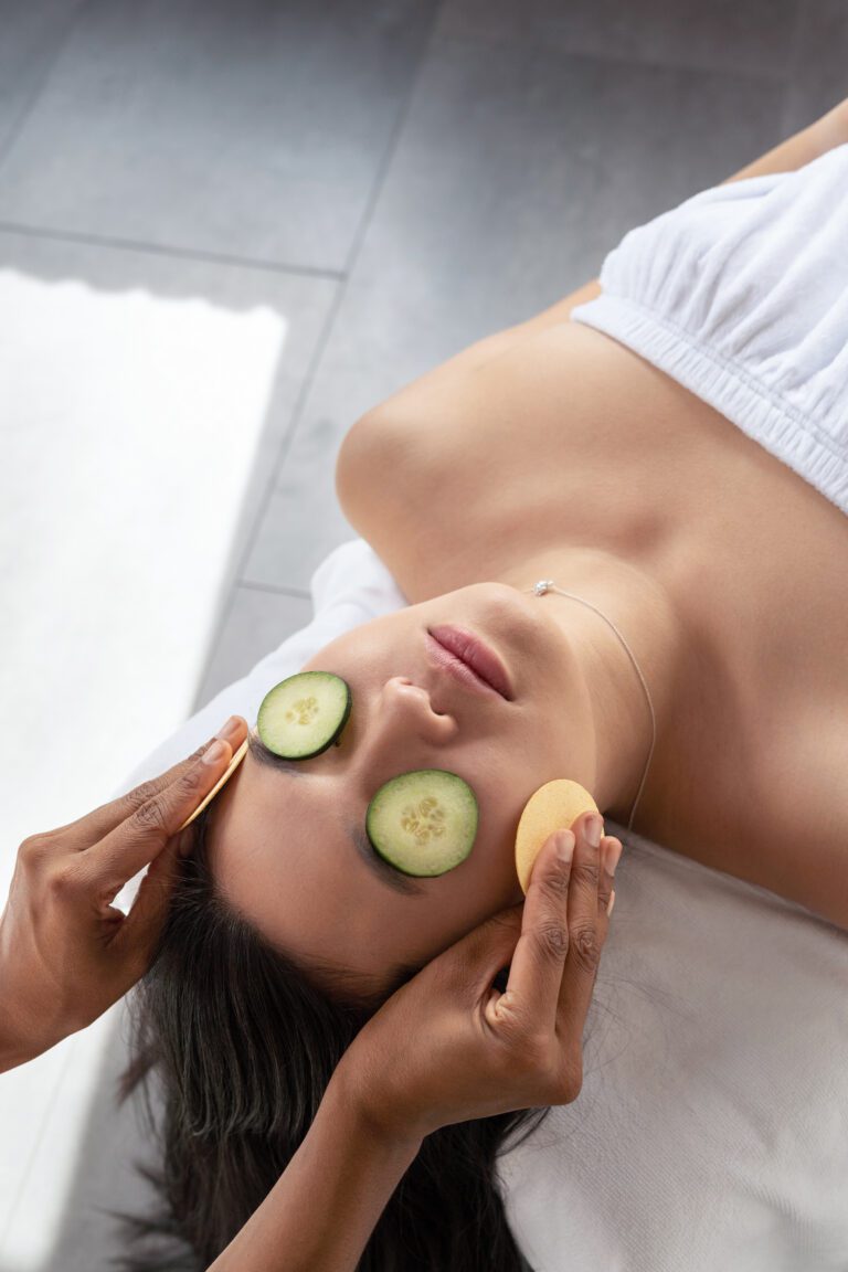 Spa facial treatment with sponges, person relaxing with cucumber slices on eyes, skincare and relaxation session.