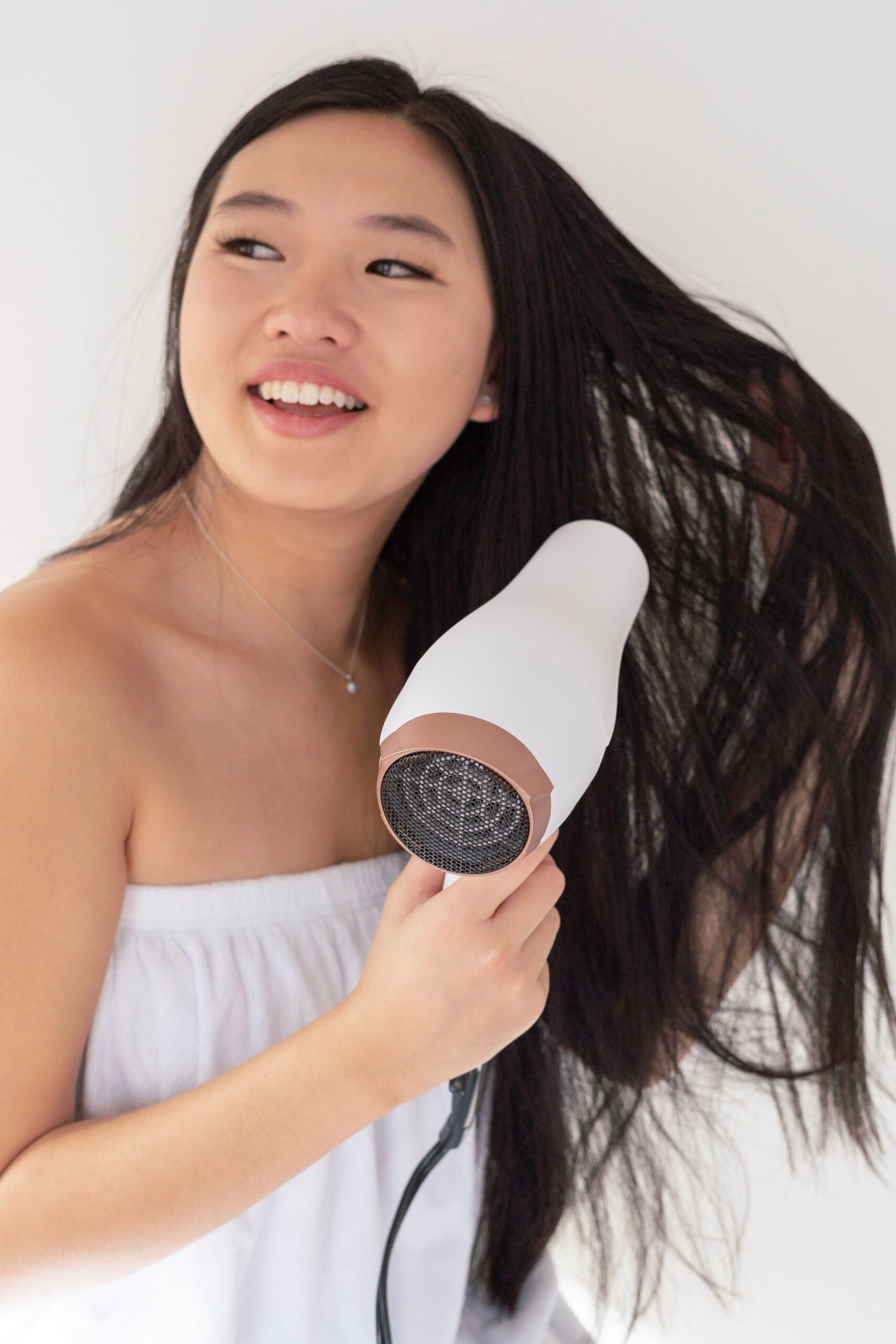 woman blow drying hair smiling during self care routine