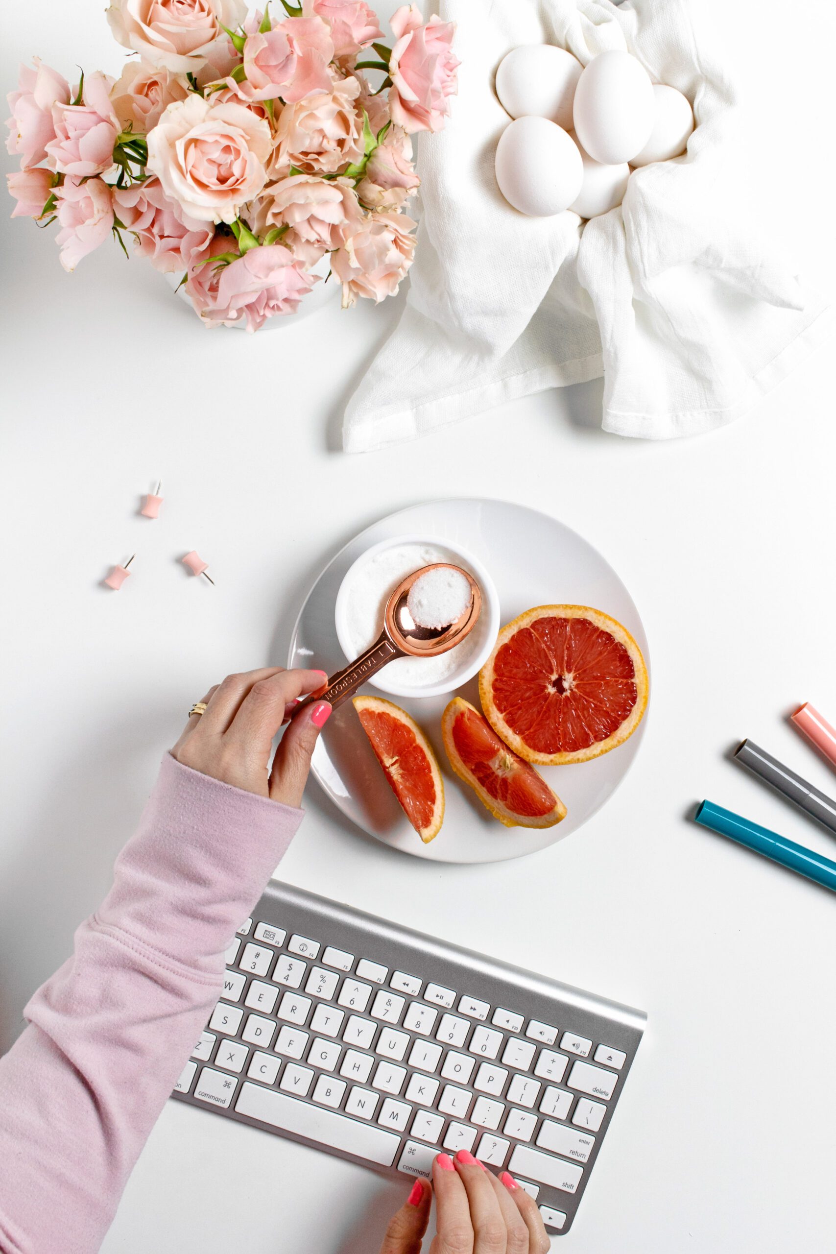 hands typing at keyboard with grapefruit plate and eggs on desk