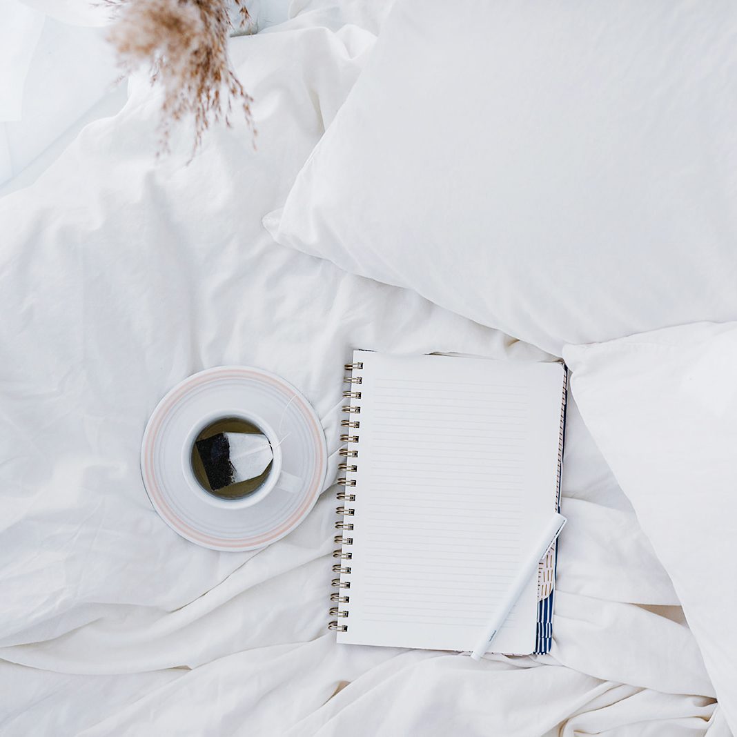 coffee and notebook on white bed morning journaling