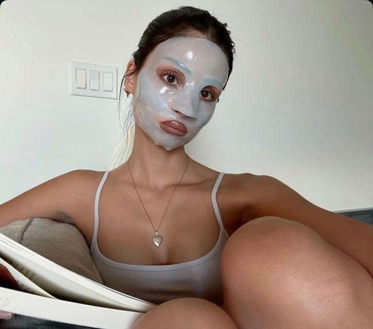woman wearing sheet mask while reading on couch