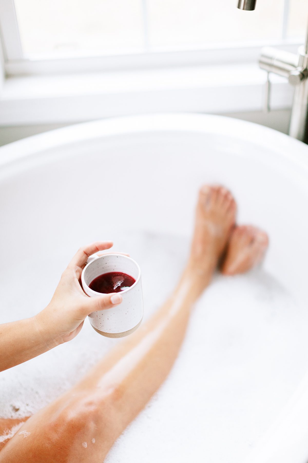 woman relaxing in bubble bath with drink summer self care routine