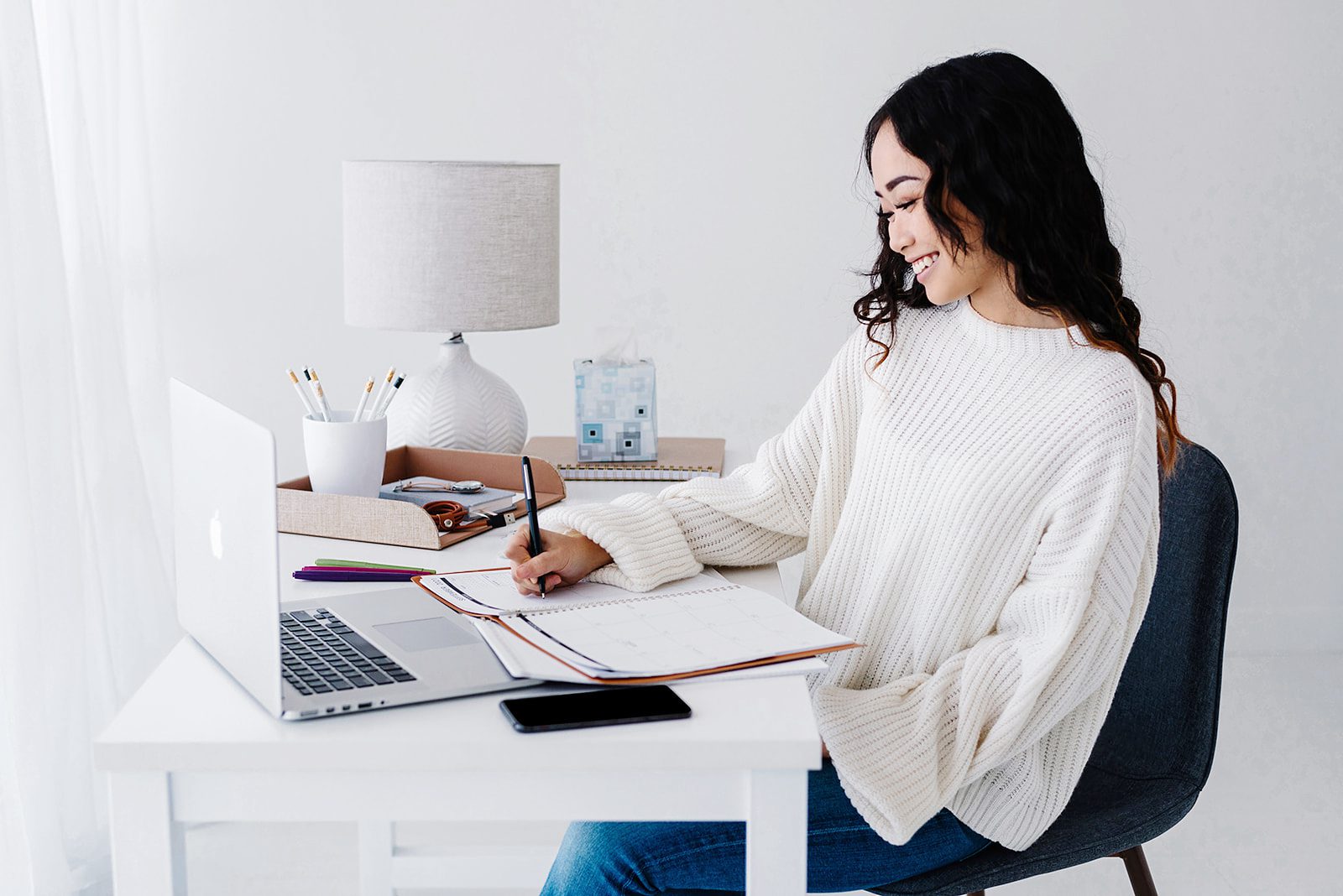 woman writing in planner at minimal desk with laptop