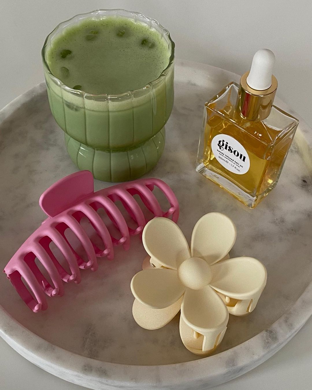 hair products flat lay with hair clips and hair oil on marble tray