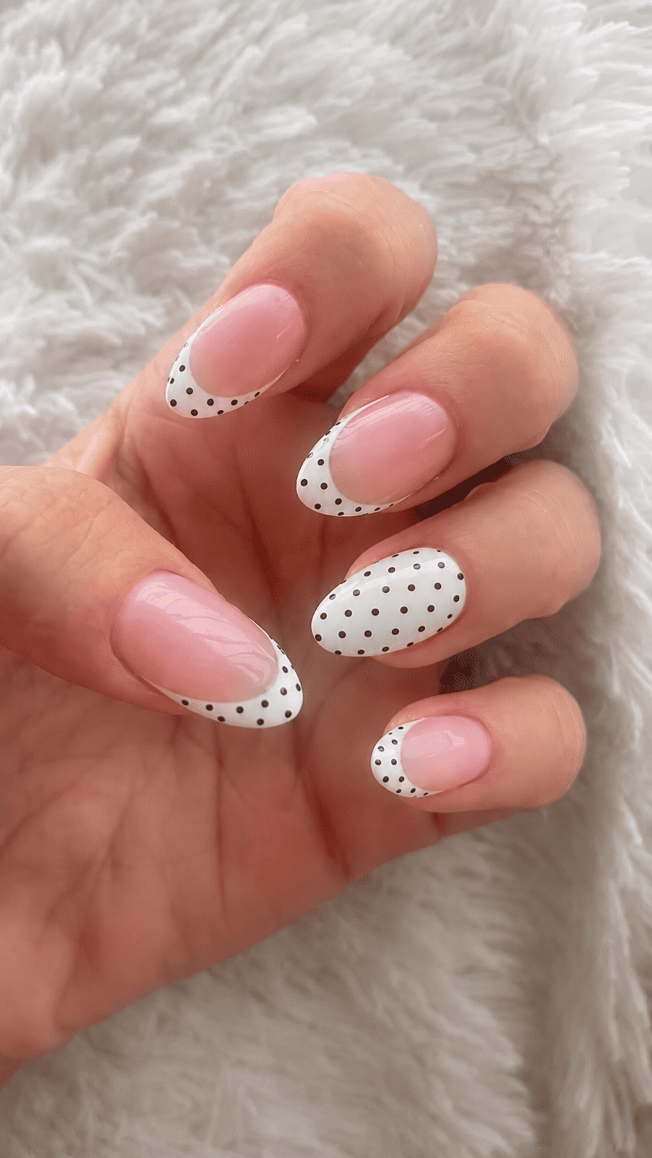 black and white polka dot French tip nails on a fluffy blanket