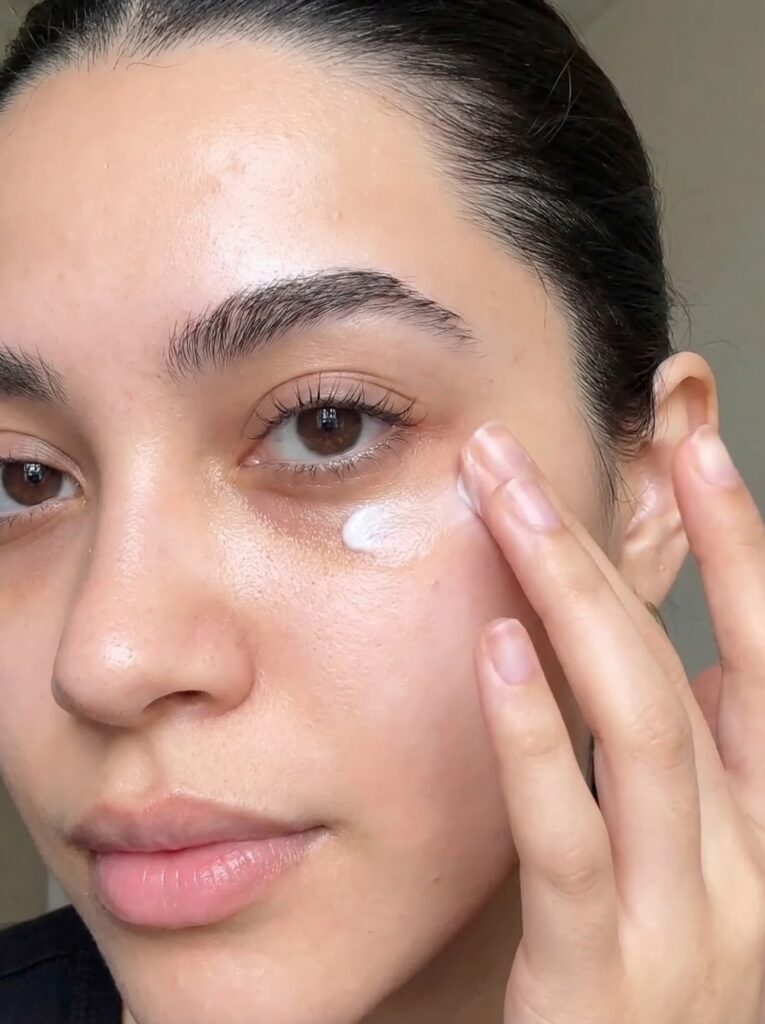 A woman gently applies top-rated eye cream for dark circles and puffiness under her eyes using her fingertip for fast results.