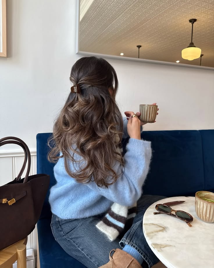 woman with long wavy hair at a cafe holding a cup