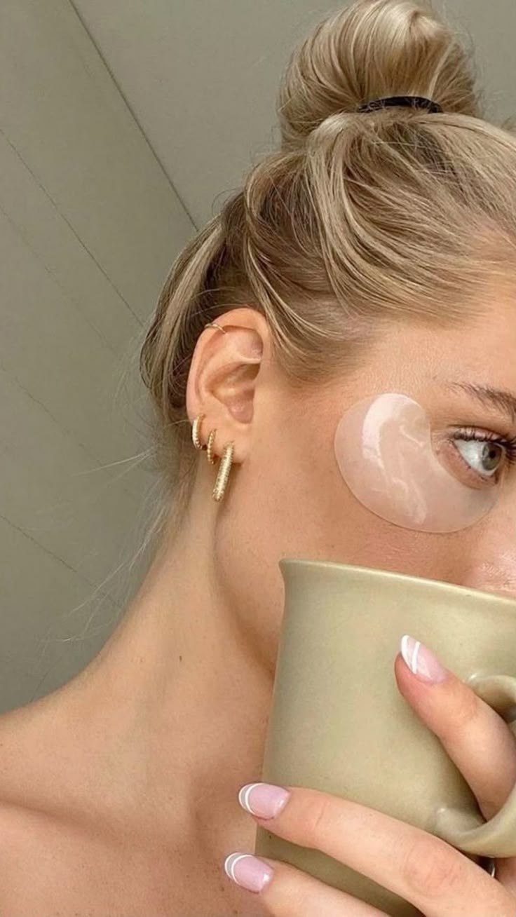woman with eye patches sipping morning coffee messy bun