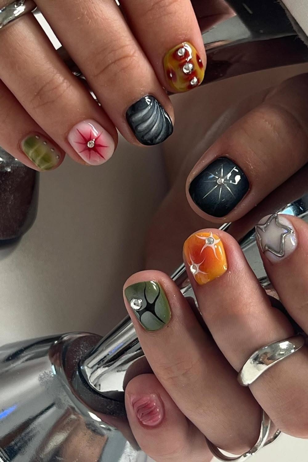 moody mismatched manicure in olive, black, and orange with tiny rhinestones