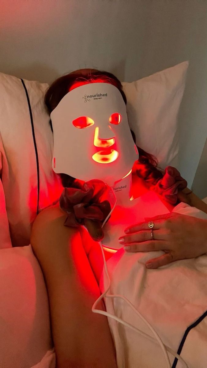 woman wearing a glowing red light therapy mask at home